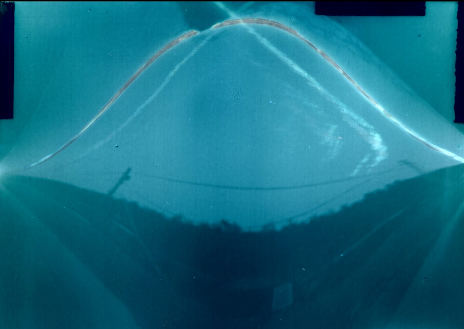 Cyanotype-toned north-aim solargraph with about 45 degree tilt showing a broad Sun arc over a bowl-shaped horizon
